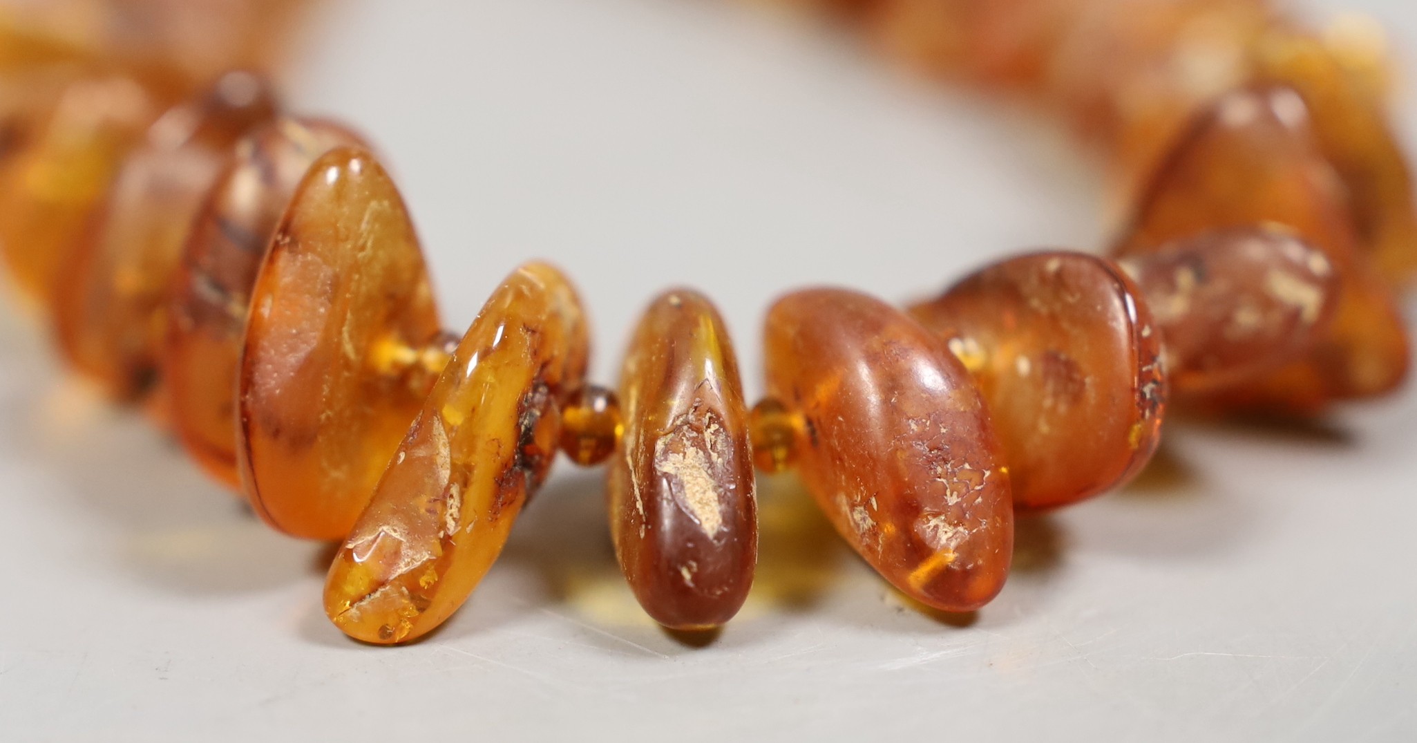 A single strand graduated amber pebble necklace, 42cm and two pairs of white metal mounted amber earrings including 925.